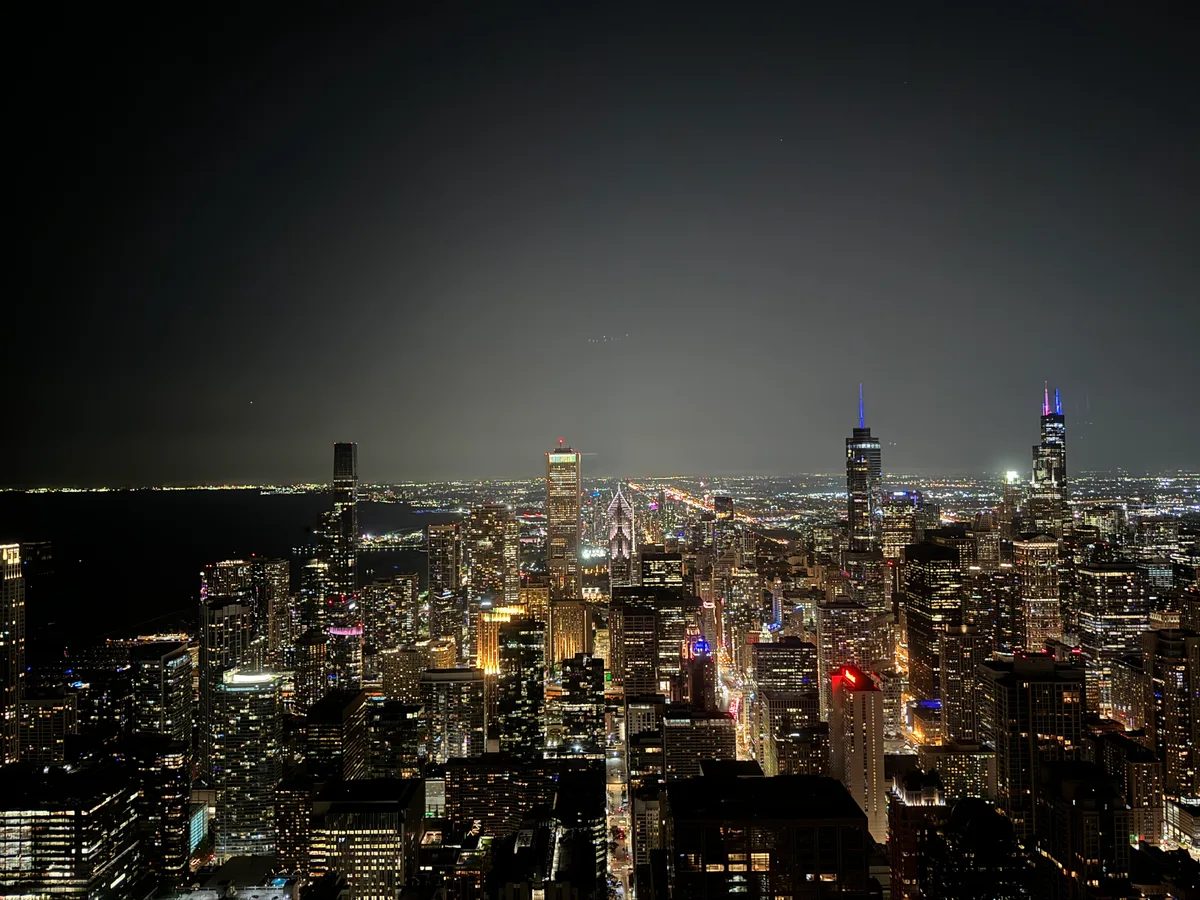 Panoramic night view of Chicago, Illinois skyline with illuminated skyscrapers including Willis Tower, and city lights stretching to the horizon above Lake Michigan
