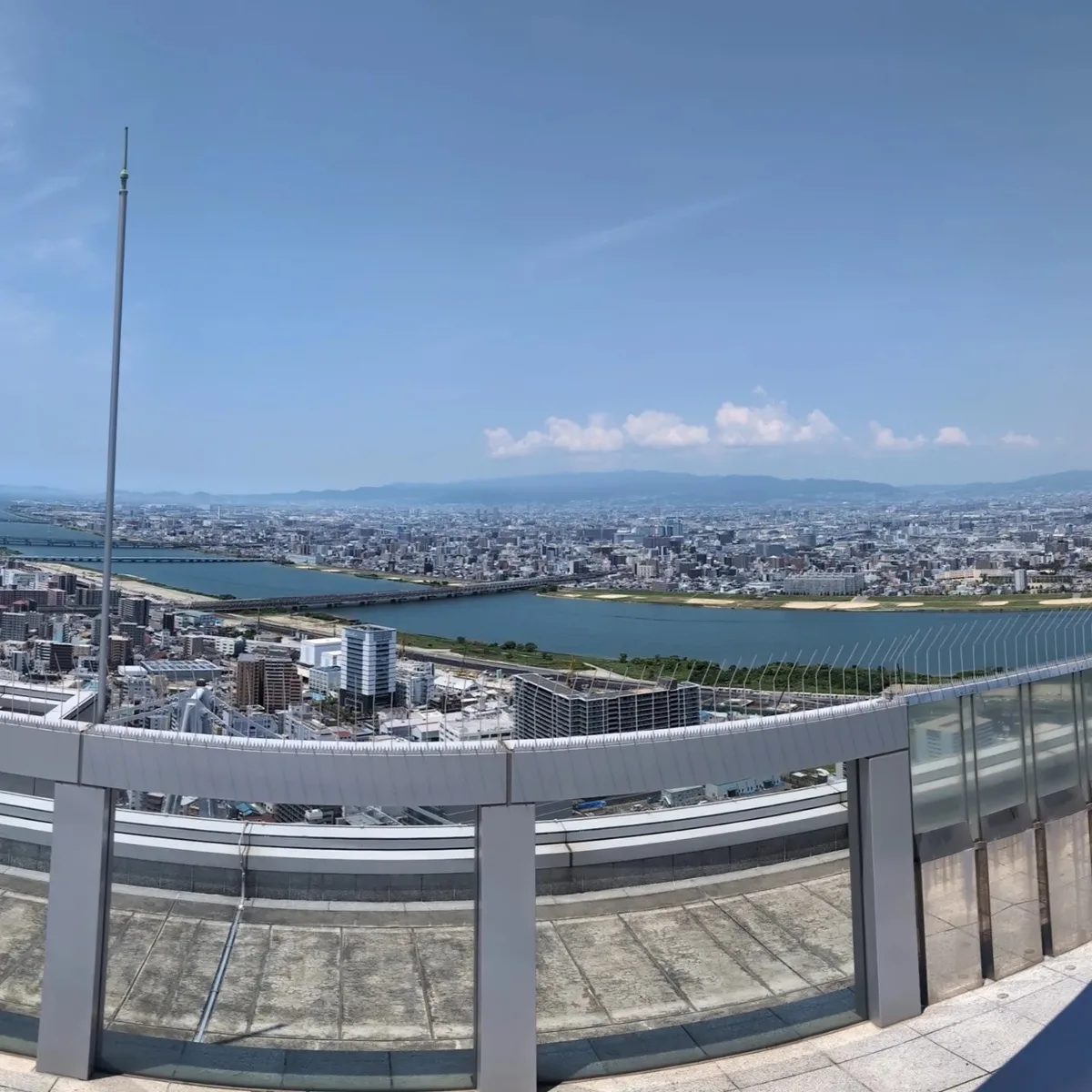 Sweeping panoramic view of Osaka, Japan from the open-air rooftop of the Umeda Sky Building, showing rivers, bridges, and the city skyline.