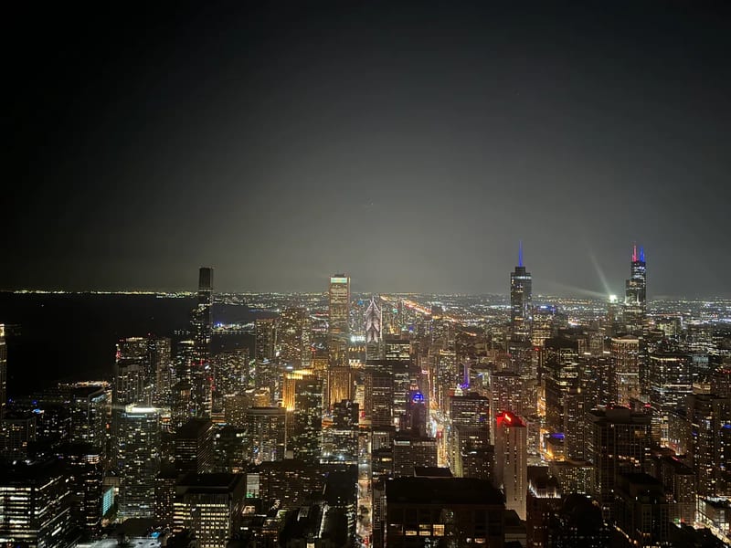 Chicago, Illinois skyline at night from the 360 Chicago observation deck on the 94th floor, with city lights illuminating skyscrapers across the Magnificent Mile