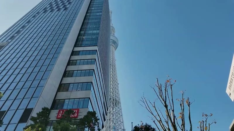Low-angle view of Tokyo Skytree rising above the surrounding glass buildings against a clear blue sky in Tokyo, Japan
