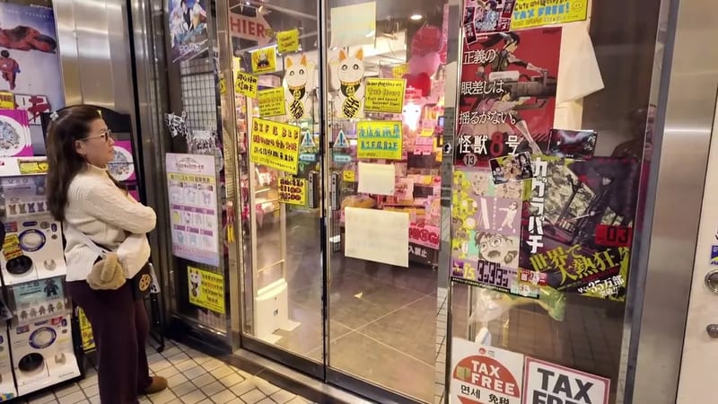 Woman browsing anime and manga merchandise through a brightly lit store window in Shibuya, Tokyo, Japan