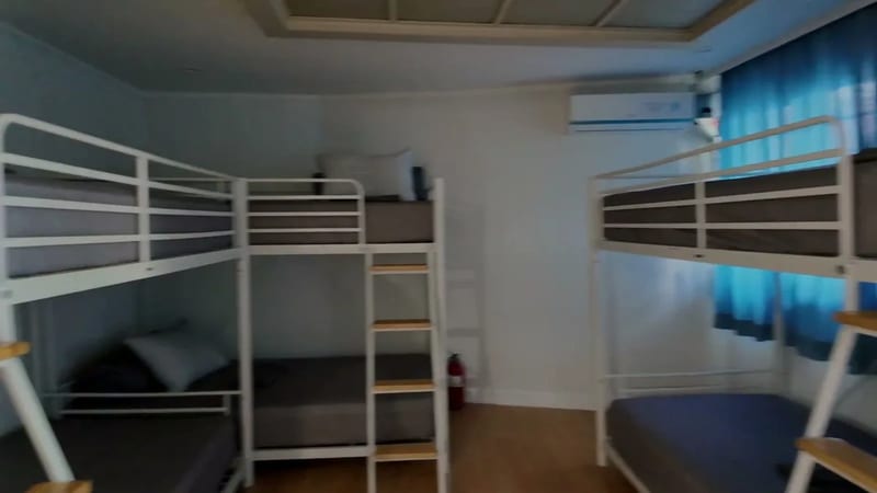 Large hostel room with several white metal bunk beds, ladders and an air conditioner