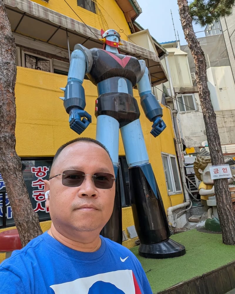 Selfie in front of a tall blue robot statue in a yellow-walled alley