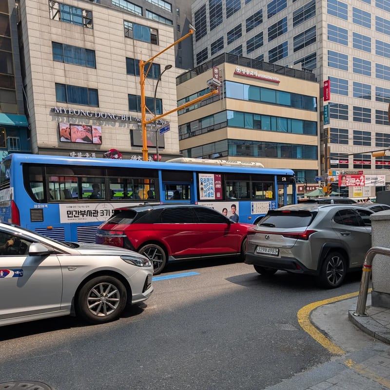 Myeongdong street traffic with a red sedan, a grey Lexus UX and a city bus
