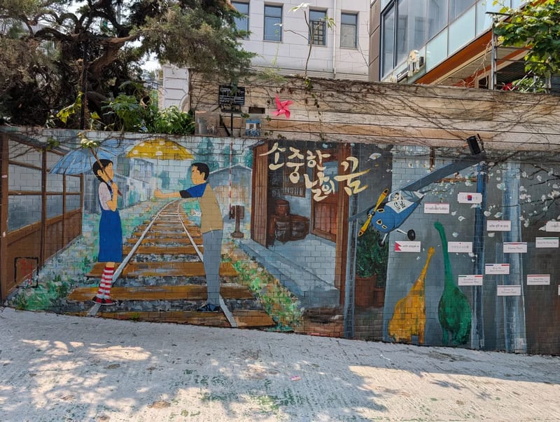Street mural of a couple meeting on train tracks under an umbrella, painted on a wall in Seoul