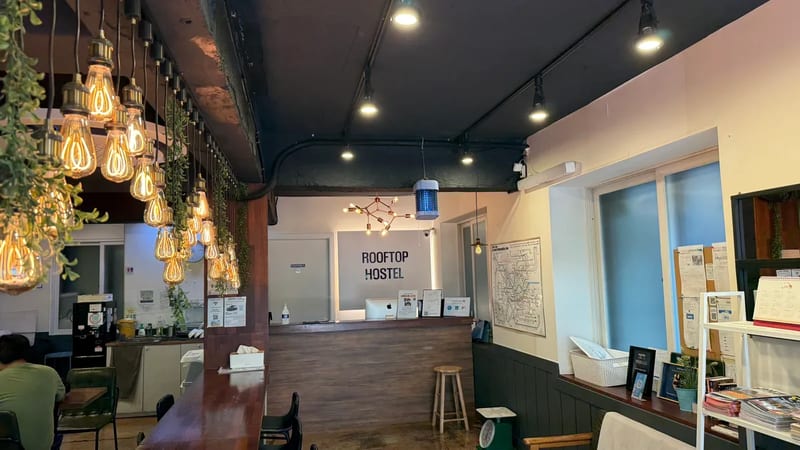 Reception of OYO Rooftop Hostel with hanging Edison bulbs, a transit map and a free breakfast counter