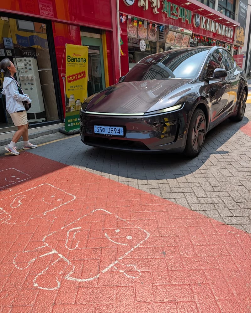 A dark grey Tesla parked on a Myeongdong side street next to chalk drawings on the pavement