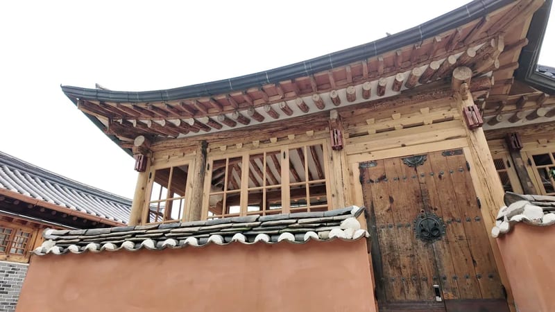 Curved tile roof and timber eaves of a hanok gate in Bukchon against a pale sky