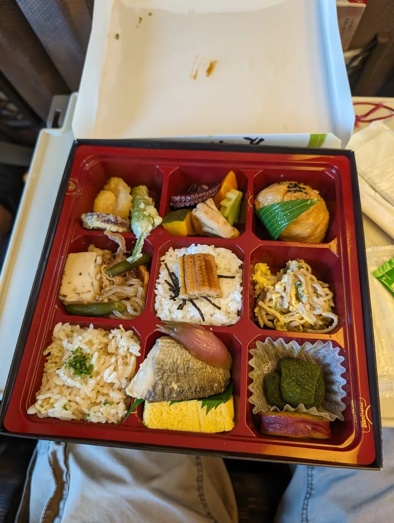 Open Japanese bento box with nine compartments of food on a Shinkansen tray table, Japan.