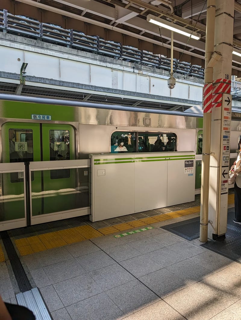 Green and silver Yamanote Line train at a Tokyo station platform with platform screen doors, Japan.