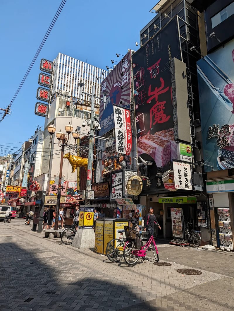 Busy street corner in Osaka, Japan, with colorful billboards, pedestrians, and a golden bull statue.