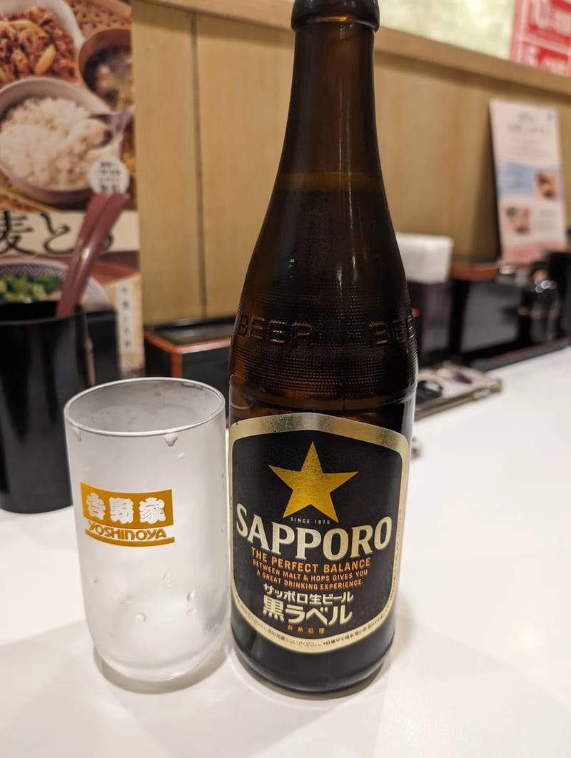 Sapporo Black Label beer bottle next to a frosted Yoshinoya-branded glass on a table in Tokyo, Japan.