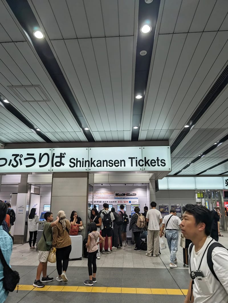 Busy Shinkansen ticket area in Shin-Osaka Station, Japan, with travelers at ticket machines and counters.