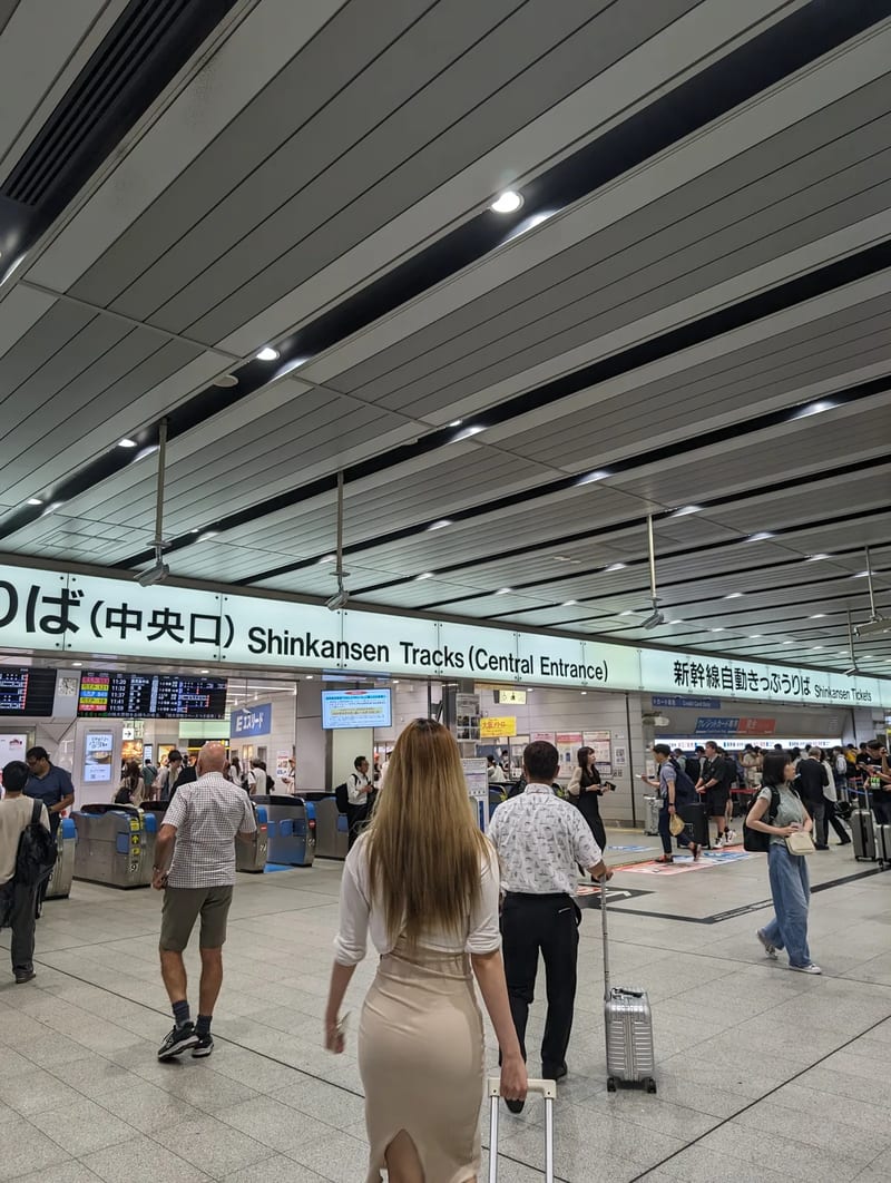 Wide Shinkansen tracks central entrance at Shin-Osaka Station, Japan, with travelers and luggage.