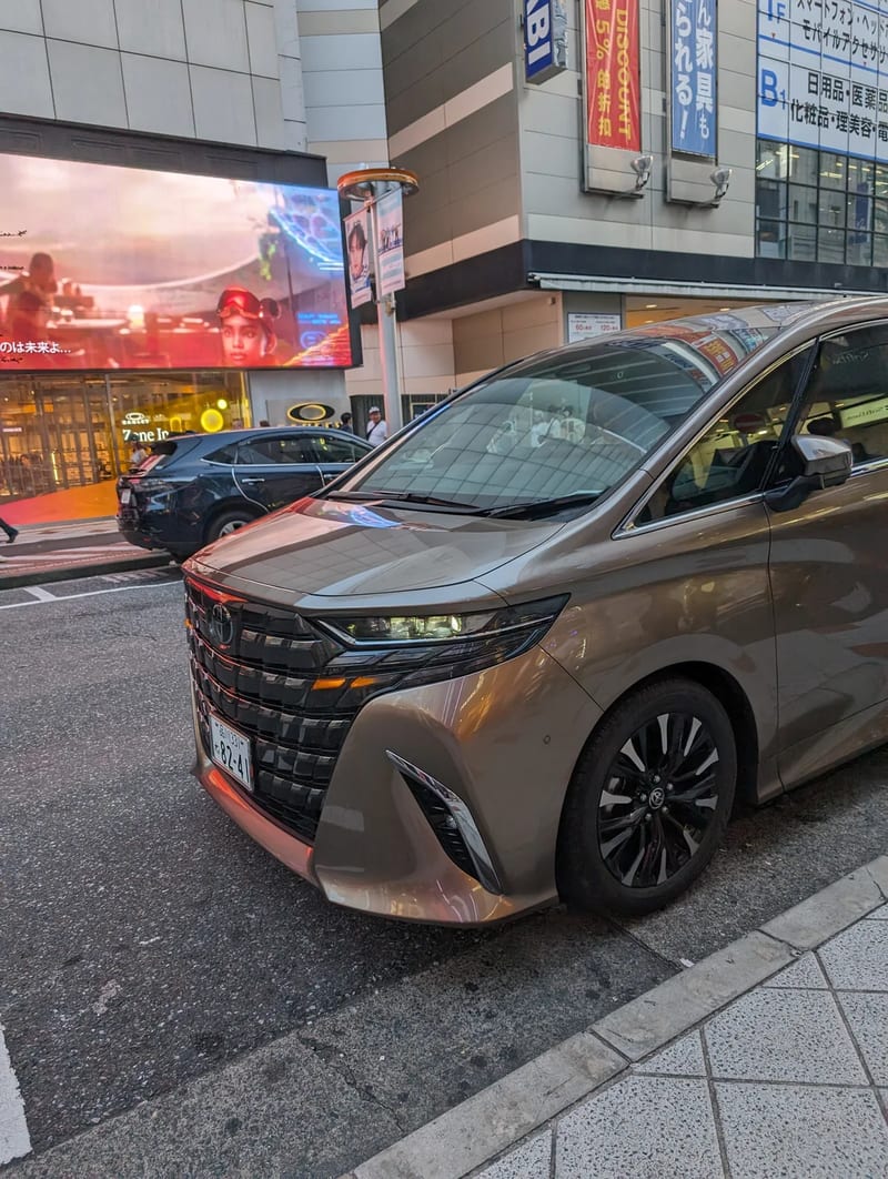 Front-side view of a gold Toyota Alphard minivan parked on a street in Shibuya, Tokyo, Japan.
