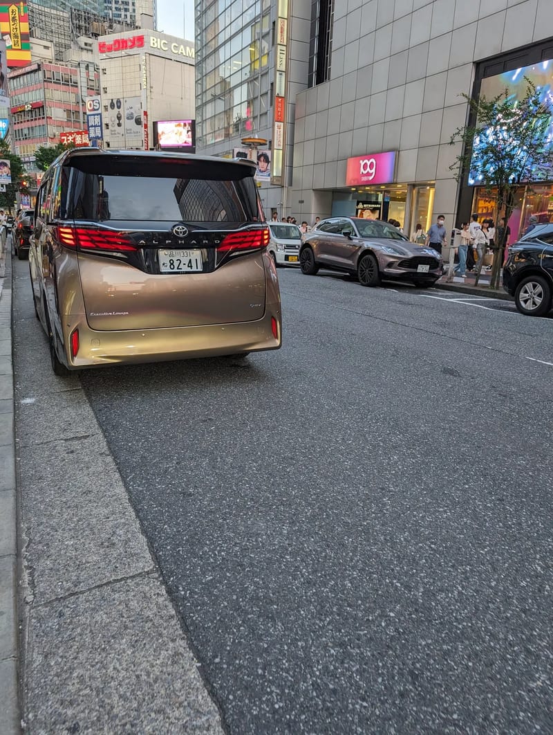 Rear view of a gold Toyota Alphard minivan parked on a street in Shibuya, Tokyo, Japan.