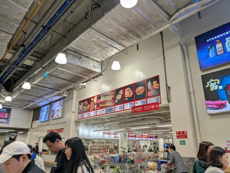 The food court menu board at Costco Yangjae in Seoul, South Korea, with the 2,000 won hot dog combo listed above the counter and shopping carts lined up below