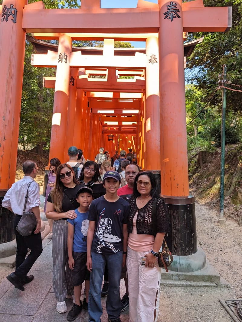 Family posing in front of orange torii gate tunnel at Fushimi Inari Shrine in Kyoto, Japan.