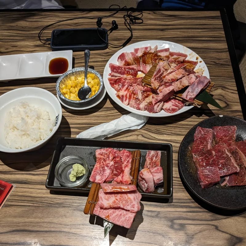 Assortment of raw beef and pork cuts, rice, and corn for Japanese BBQ on a wooden table.
