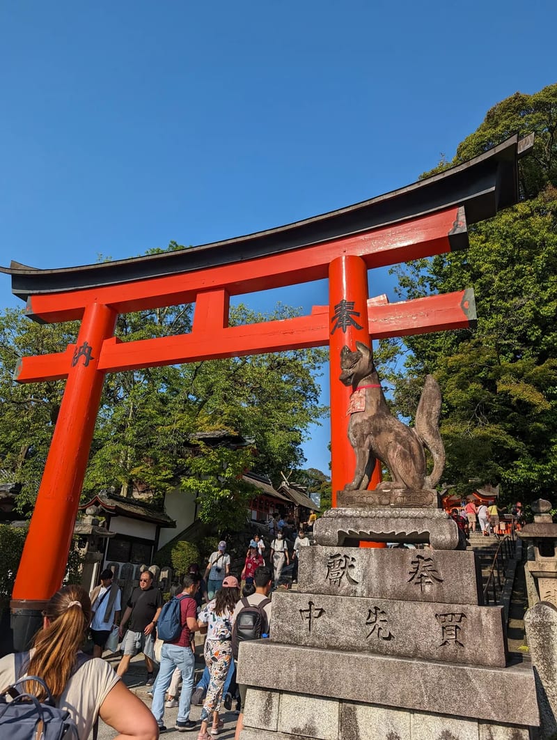 Large red torii gate and stone fox statue at a Japanese shrine entrance in Kyoto, Japan.
