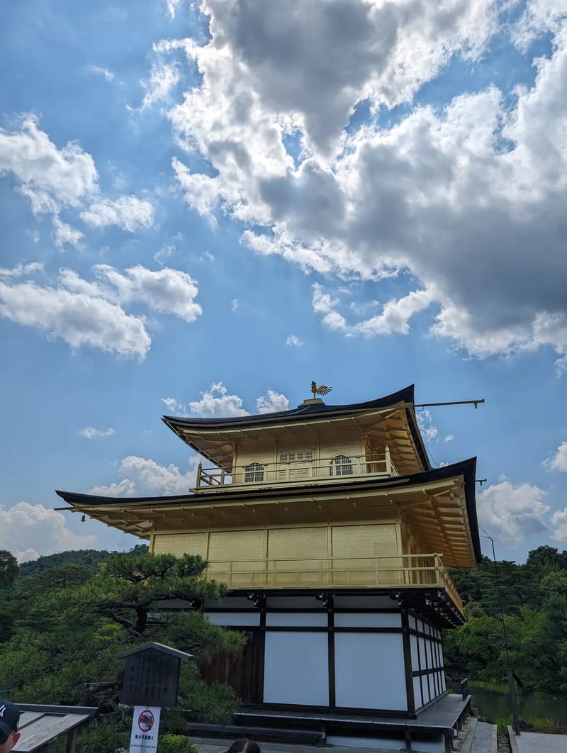 Side view of Kinkaku-ji Golden Pavilion with golden and white sections under a blue sky in Kyoto, Japan.