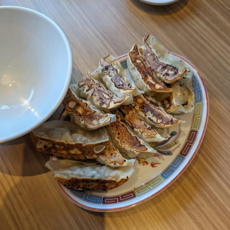 Plate of pan-fried gyoza dumplings with crispy bottoms on a wooden table in Japan.