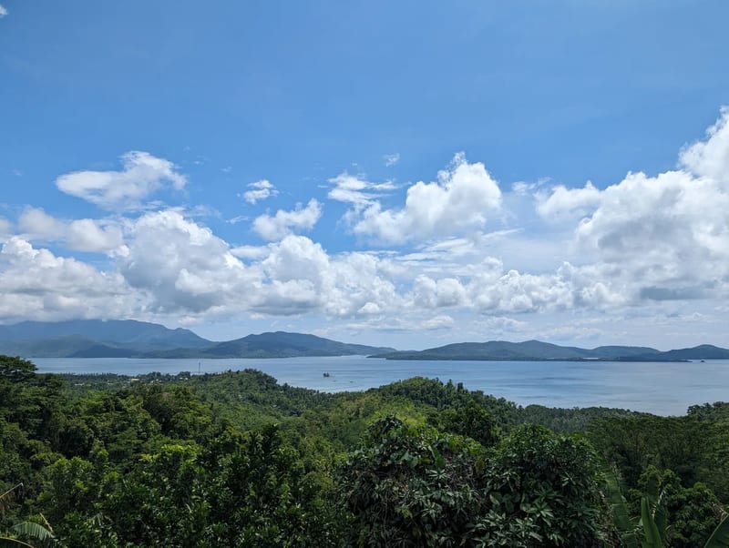 Panoramic view of a bay dotted with islands surrounded by lush green hills under a bright blue sky with white clouds on the road between Sabang and Puerto Princesa, Palawan, Philippines