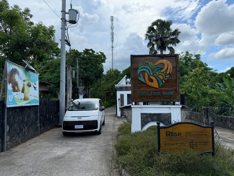 Wooden Good Food Farm entrance sign with a green and gold logo beside a white van at the gate
