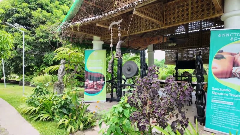 The Sanctuario Spa pavilion on the grounds Open thatched spa pavilion with hanging gongs and Sanctuario Spa banners in the garden