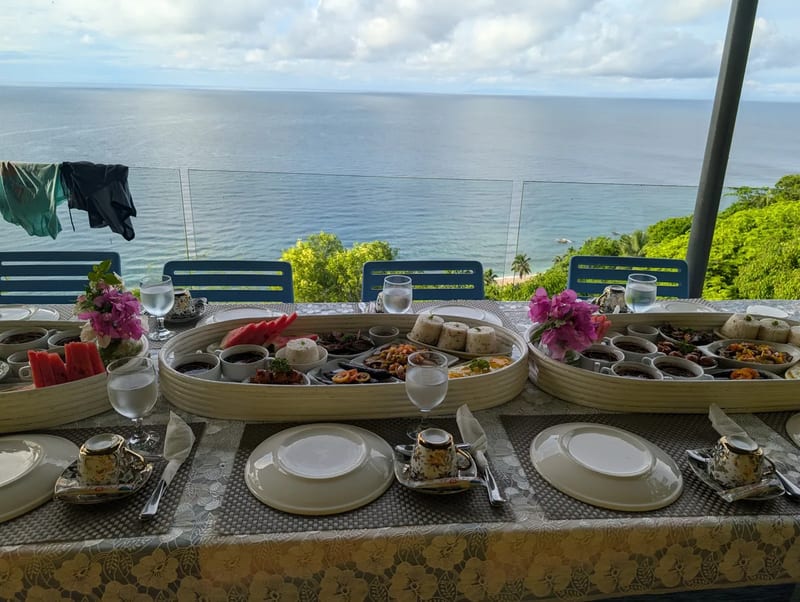 Two large oval platters of breakfast food with rice, eggs, and fruit on an outdoor table with the ocean in the background at Casa Amara, Batangas, Philippines.