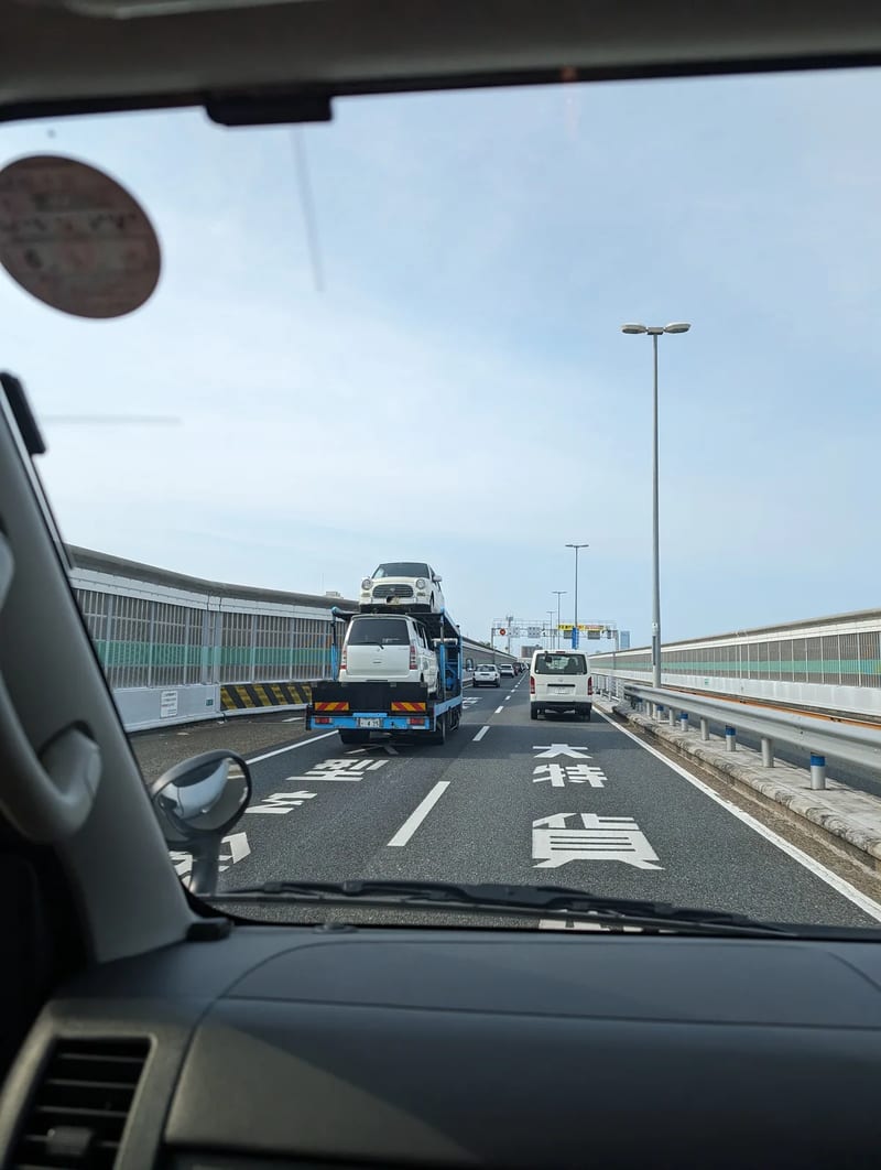 Car carrier truck transporting two white SUVs on a Japanese highway in Osaka.