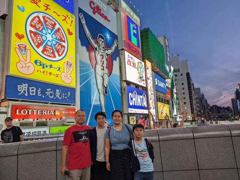 Family of four in front of the Glico Man sign from a wide angle at dusk in Dotonbori, Osaka, Japan.