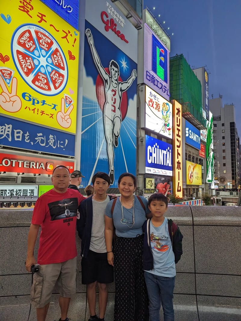 Family of four posing in front of the iconic Glico Man sign in Dotonbori, Osaka, Japan.