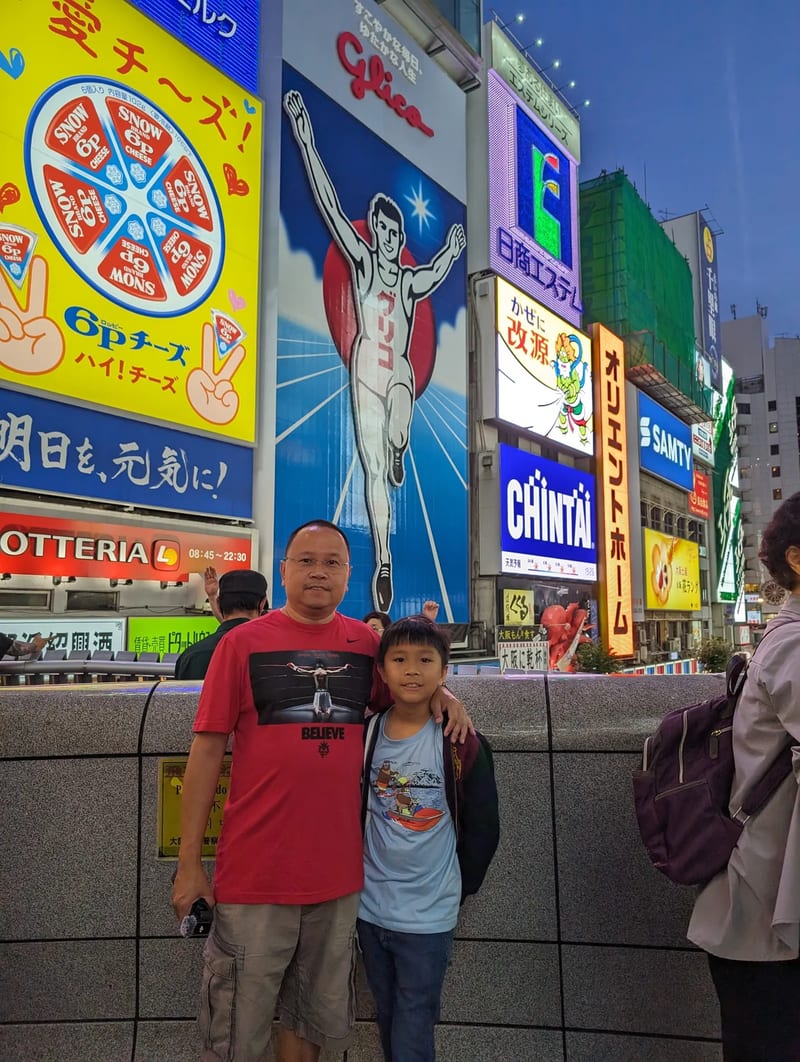 Father and son posing in front of the iconic Glico Man sign in Dotonbori, Osaka, Japan.