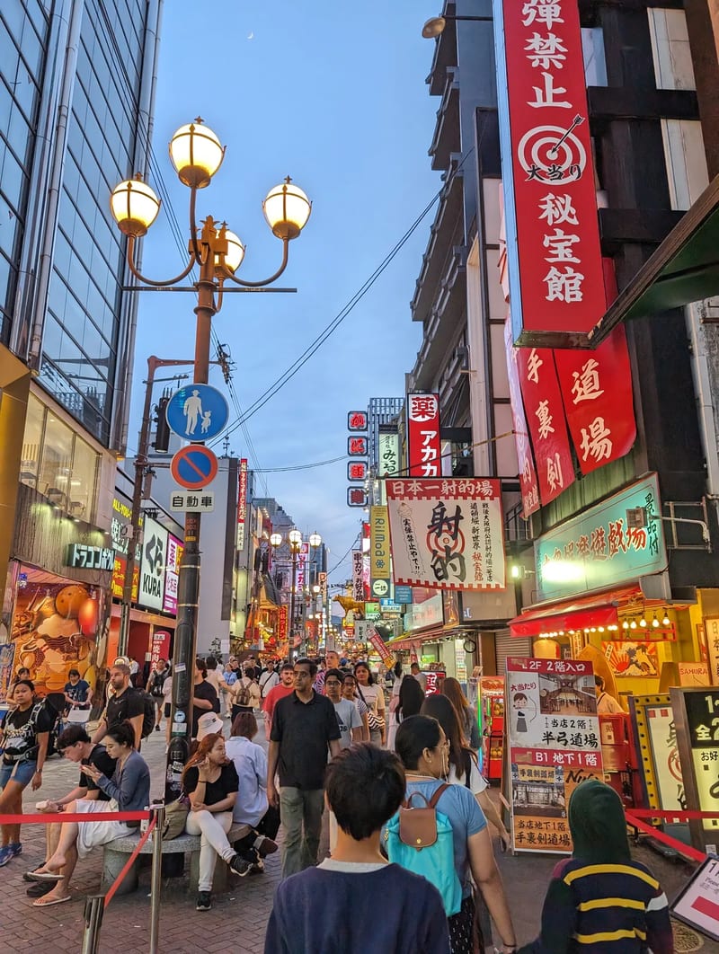 Lively Dotonbori street scene in Osaka, Japan with pedestrians and bright neon signs and lanterns.