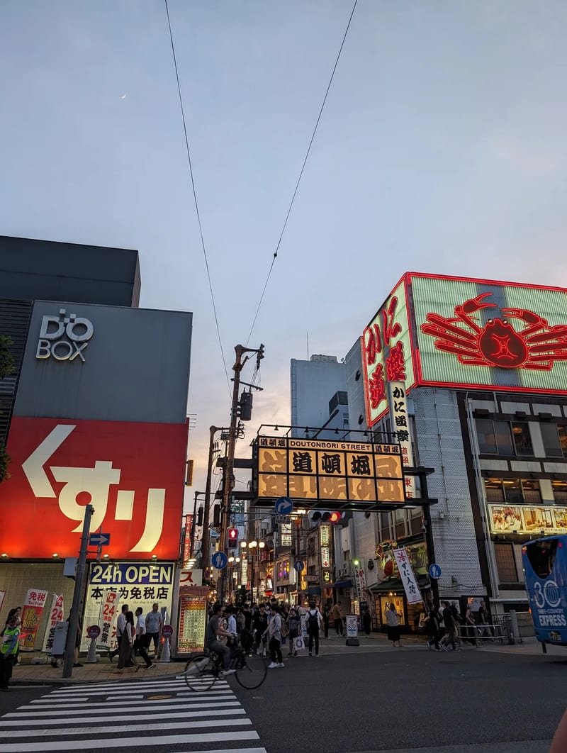 Wide view of Dotonbori street in Osaka, Japan at dusk with neon signs and pedestrians.