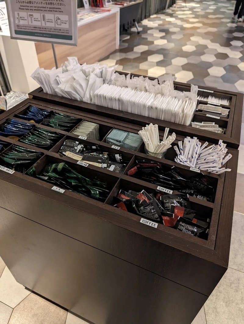 Hotel coffee and tea amenity station with various packets and stirrers at Sotetsu Grand Fresa in Osaka, Japan.