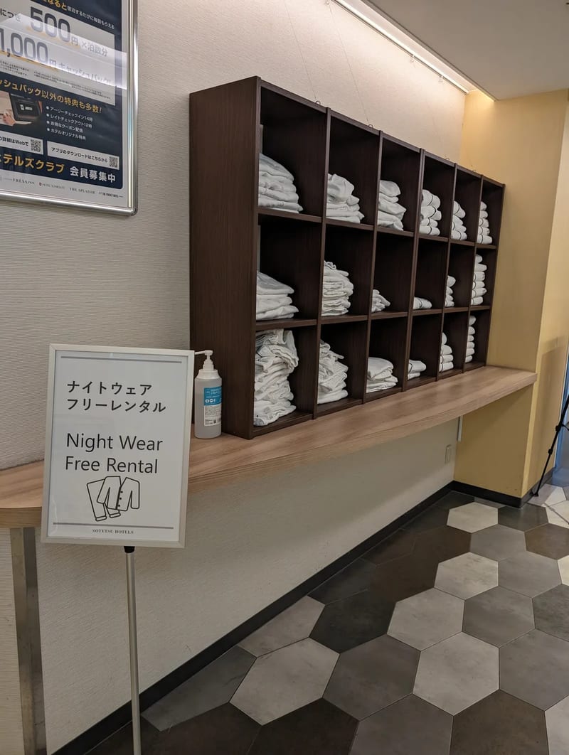 Hotel lobby shelf with free nightwear for rental and a sign at Sotetsu Grand Fresa, Osaka, Japan.