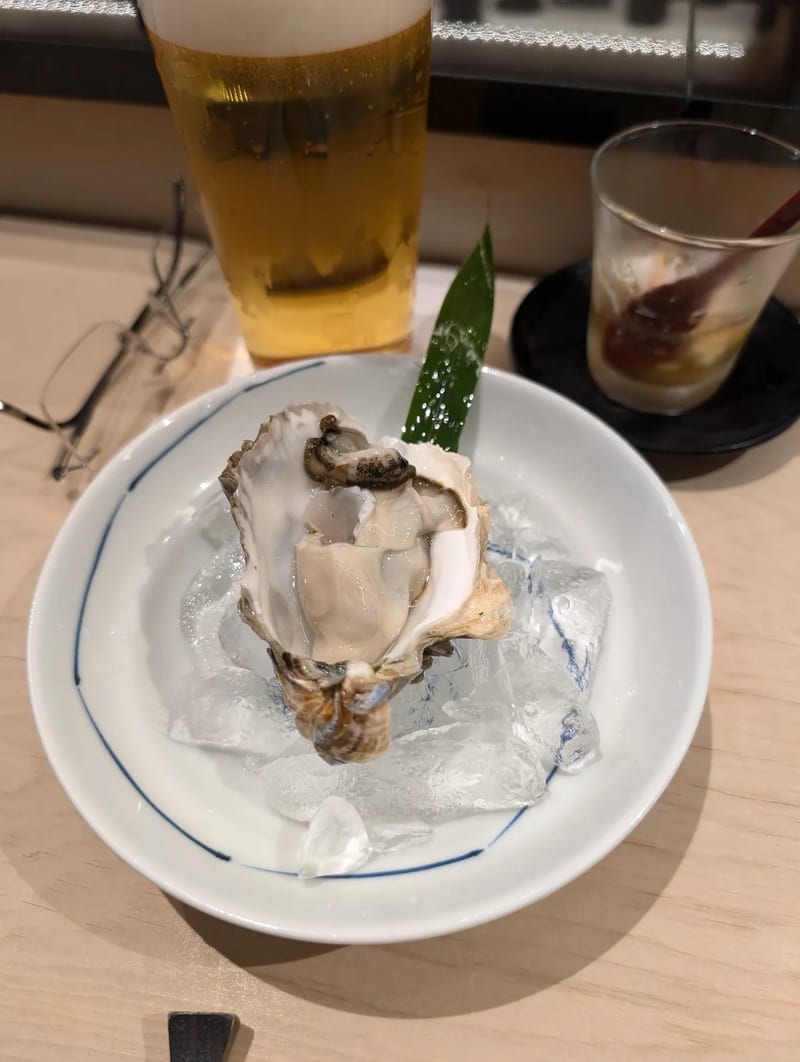 Fresh oyster served on a bed of ice in a white and blue rimmed bowl, garnished with a green leaf, at an omakase restaurant in Shibuya, Tokyo, Japan.