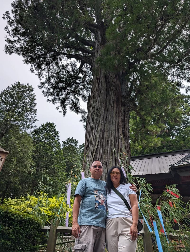 Couple standing next to the sacred tree at Fuji Sengen-Jinja Shrine, Fujiyoshida, Yamanashi, Japan.