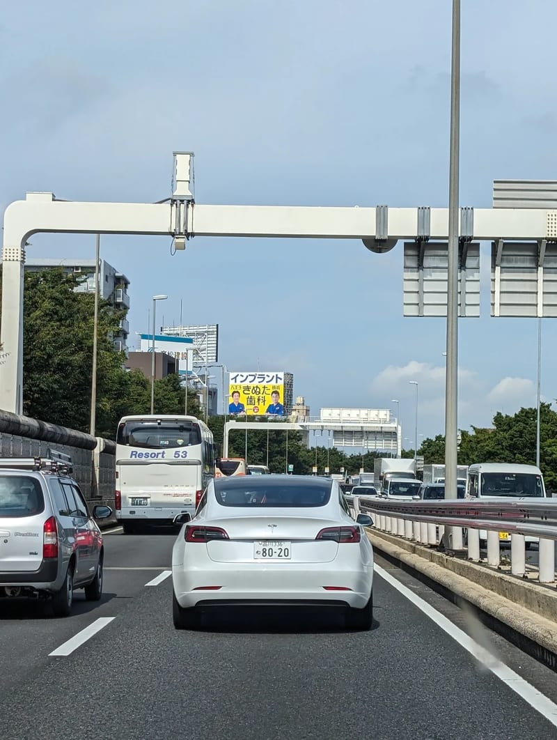 Spotting Teslas on the Tokyo expressway — they're here, just fewer than back home White Tesla on a multi-lane Tokyo expressway in Japan under a clear blue sky.
