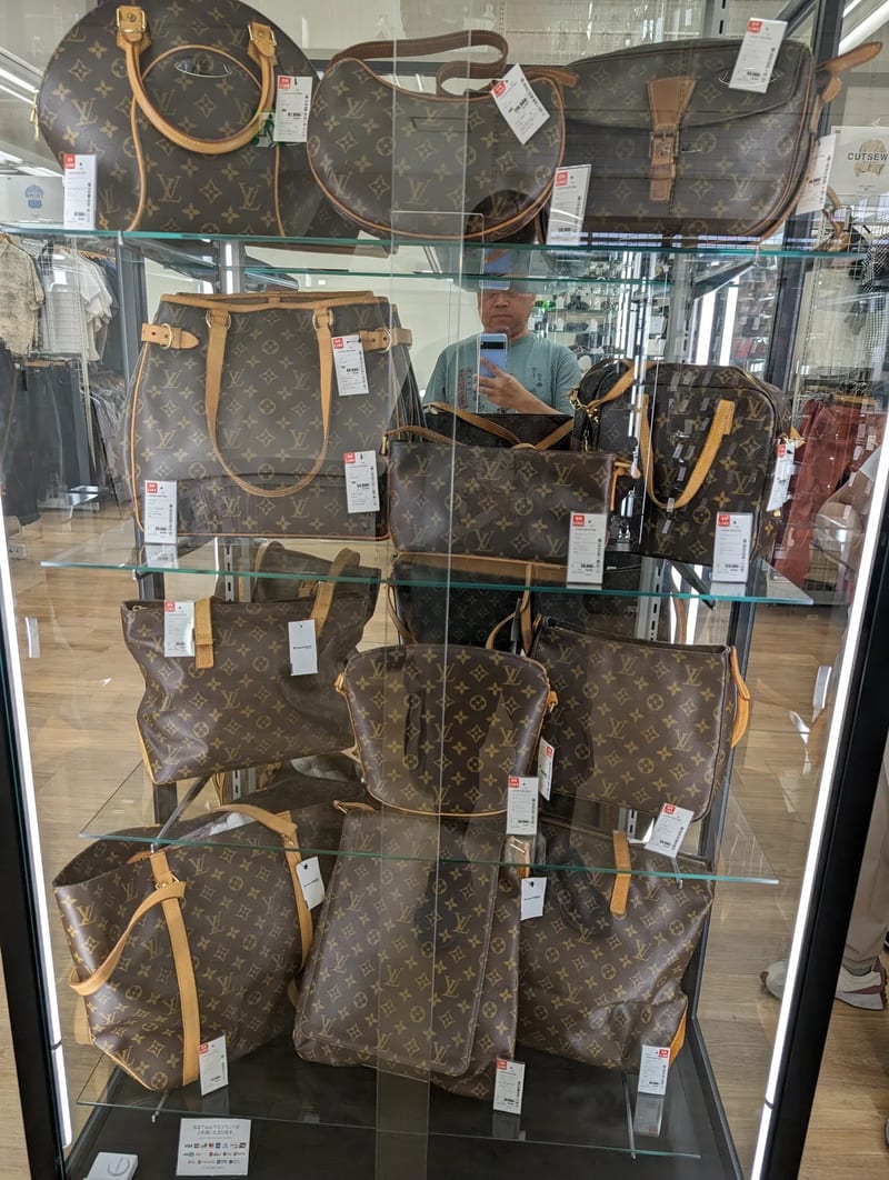 Louis Vuitton handbags displayed behind glass at a Japanese resale store.