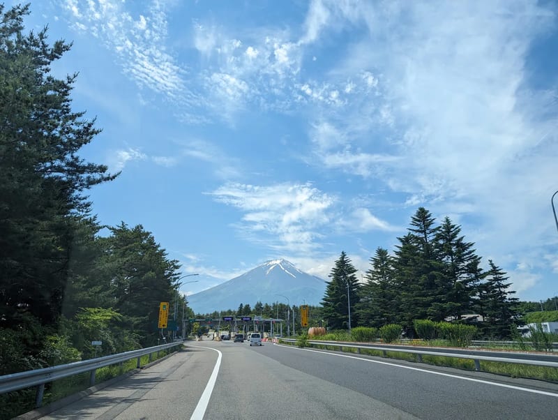 Closer view of road to toll booth framed by pine trees with Mount Fuji behind, Yamanashi, Japan.