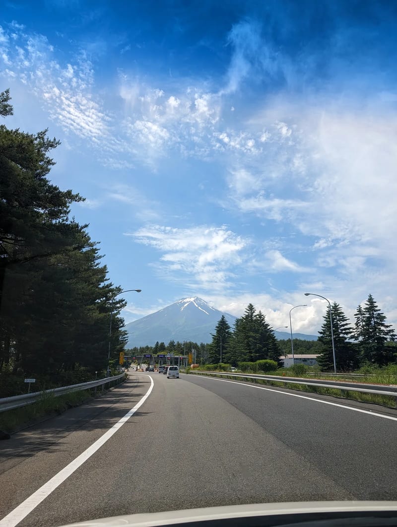 Road approaching a toll booth with Mount Fuji and tall pine trees in Fujiyoshida, Yamanashi, Japan.