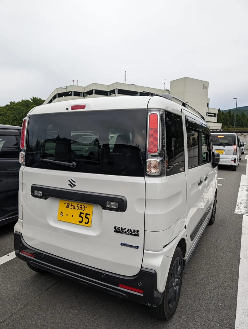 Rear view of white Suzuki Spacia Gear kei car in a parking lot in Japan.
