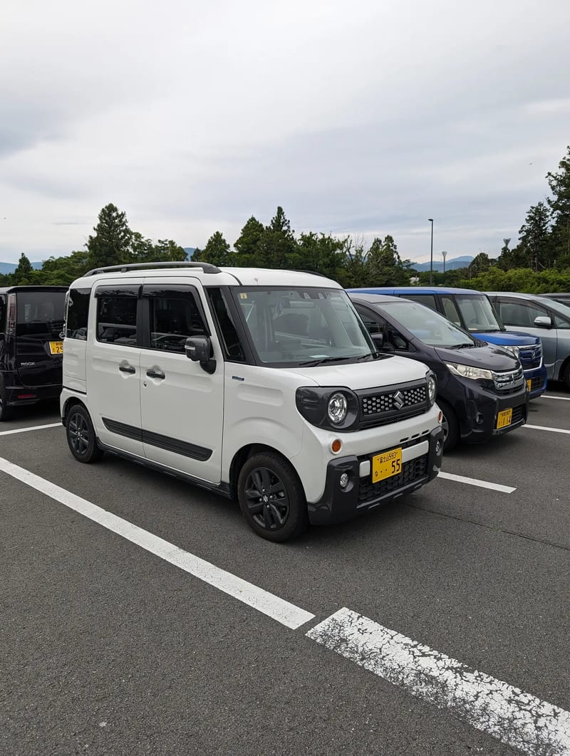 White Suzuki Spacia Gear kei car parked in a lot in Japan.