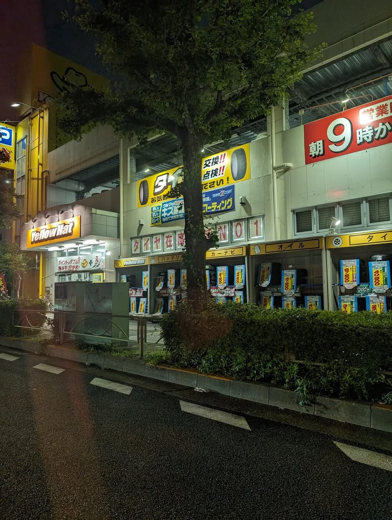 Yellow Hat auto store at night in Japan — I wanted to go in. We did not go in. Yellow Hat auto parts store illuminated at night in Japan.