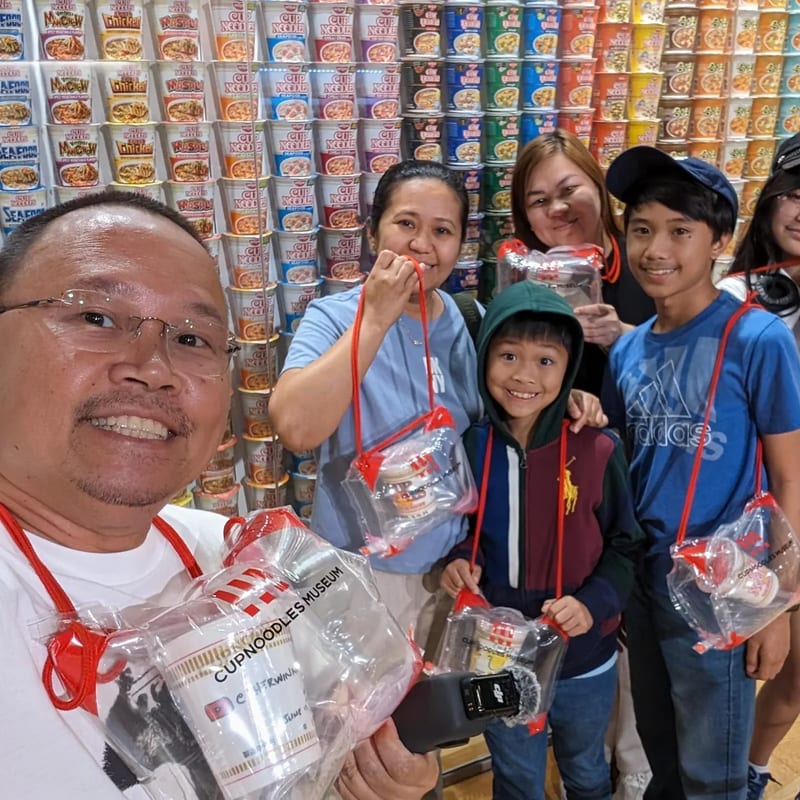 Family selfie at Cup Noodles Museum noodle wall exhibit in Osaka, Japan.