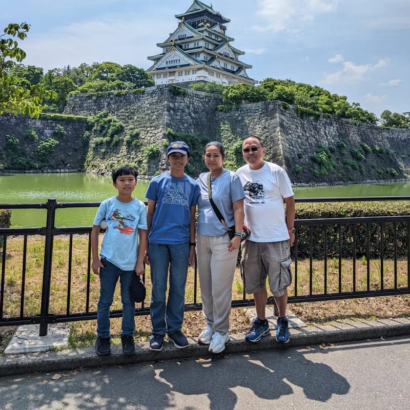 Family of four posing in front of Osaka Castle moat and stone walls in Osaka, Japan.