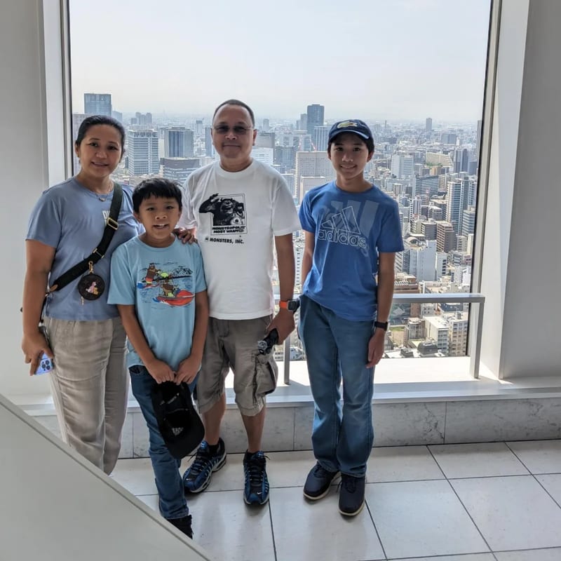 Family at Umeda Sky Building observation deck window with panoramic Osaka city view, Japan.